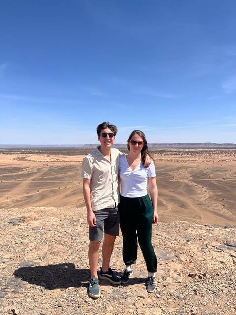       Smiling couple pose with sweeping desert escarpment in background.
  