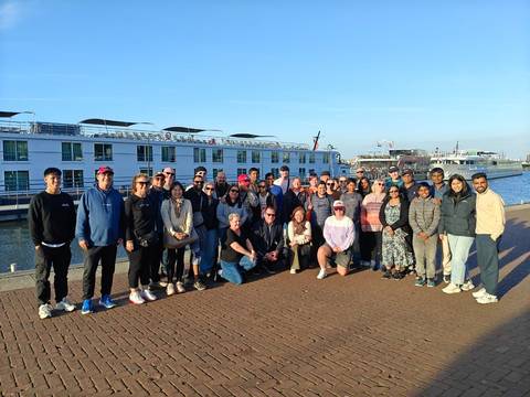       Tour group stands on dock beside river cruise ship under clear sky.
  