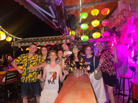       Colorful night-time bar scene with young travelers in patterned shirts posing.
  