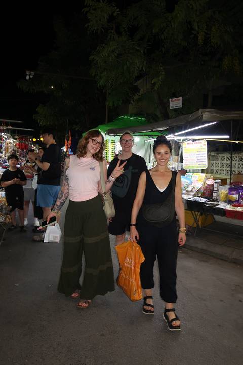       Travelers smile while browsing vibrant night market stalls.
  