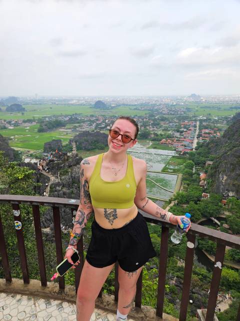       Young woman posing at a high scenic lookout over green rice fields, karst peaks and villages.
  