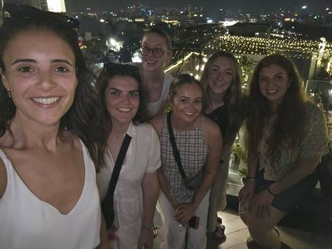       Six friends posing on a rooftop bar at night with strings of decorative lights in the background.
  