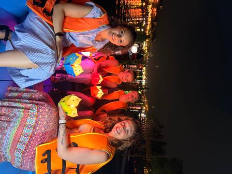       Four women in life jackets holding colorful paper lanterns while sitting in a small boat on a river at night.
  