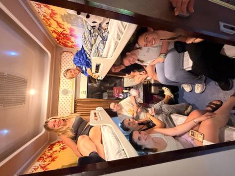       Nine travellers sitting and chatting in a narrow sleeper train cabin with bunk beds.
  