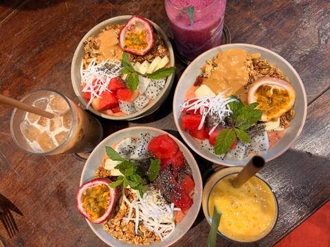       Overhead shot of colorful fruit smoothie bowls and iced drinks on a wooden table.
  