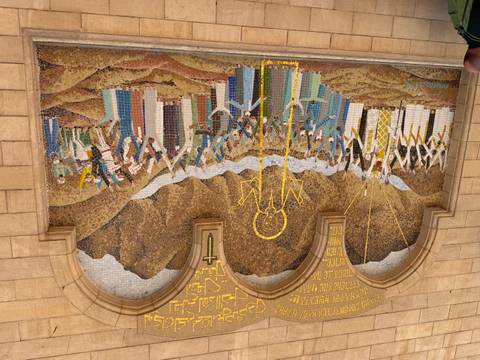       Large colorful mosaic mural depicting a biblical scene on a stone church wall.
  