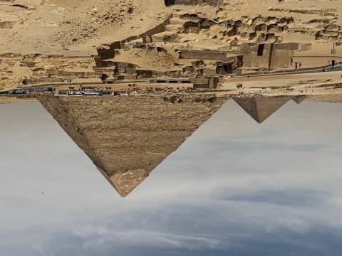       Panoramic desert vista of the Great Pyramid and nearby pyramids beneath a hazy sky.
  