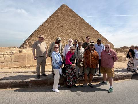       Tour group poses in front of one of the Giza pyramids on a bright day.
  
