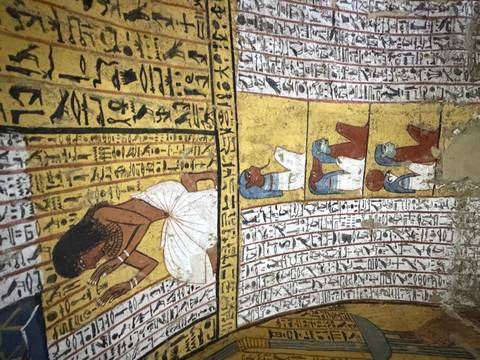       Colorful frescoes and hieroglyphs depicting ancient Egyptian figures line the curved walls of a tomb chamber.
  