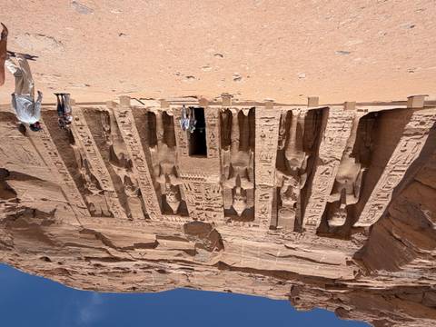       Facade of the Small Temple at Abu Simbel carved into sandstone cliffs with colossal statues and visitors at its base.
  