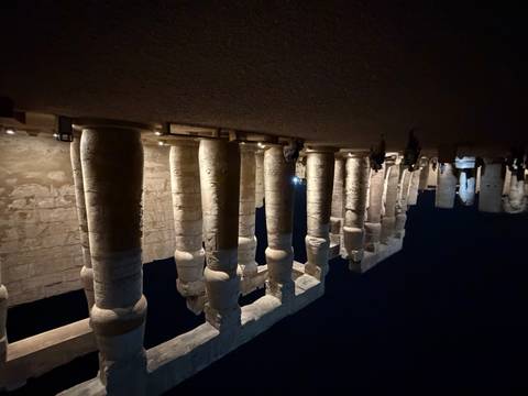       Massive illuminated columns of Luxor Temple at night with visitors walking among them.
  