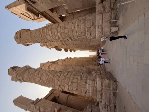       Visitors walk between towering sandstone columns of Karnak temple's great hall in soft late-day light.
  