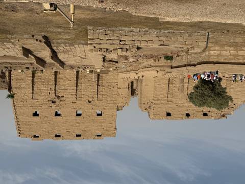       Ruined walls and ram-headed sphinx avenue of Karnak Temple with a cluster of tourists on the left.
  