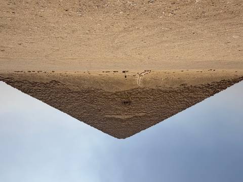       The Red Pyramid stands alone in the desert under a hazy sky with the entrance ramp visible at its base.
  