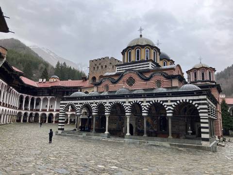       Striped black-and-white arcaded façade of Rila Monastery surrounded by forested mountains.
  