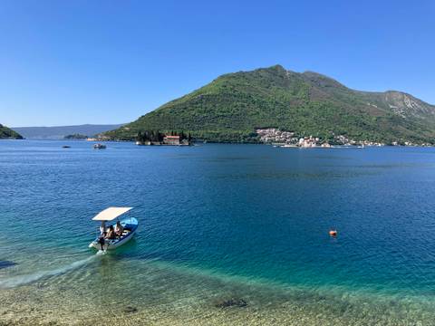       Serene blue bay with boat and green mountains; tiny church islands visible offshore.
  