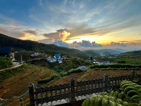       Golden-hour view of a hill village and patchwork farms under a dramatic sunset sky.
  