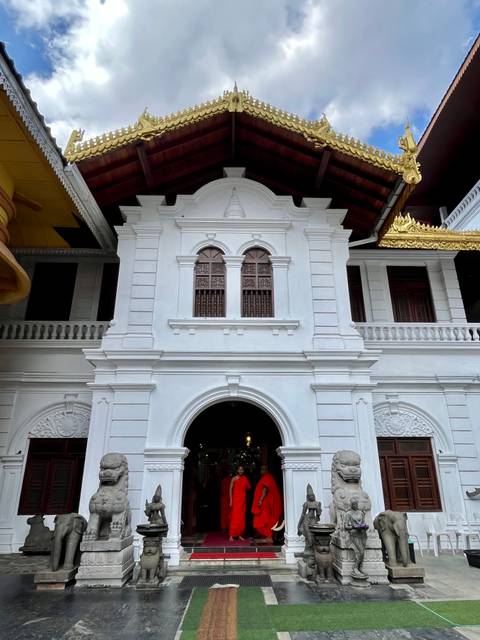       White colonial-era façade with arched doorway and ornate windows of a Sri Lankan temple.
  