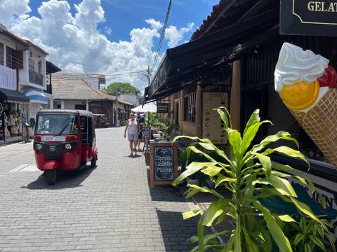       Cobblestone street in Galle Fort with tuk tuk, tourists, shops and a giant ice-cream cone sign.
  