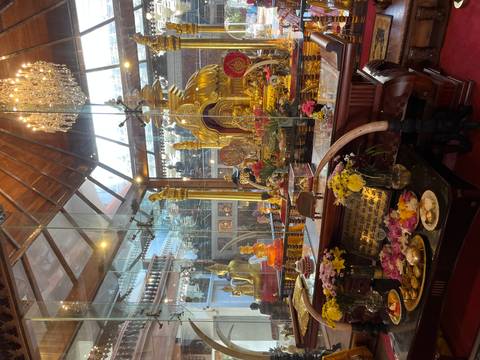       Opulent Buddhist shrine filled with golden statues, flowers and offerings behind glass.
  