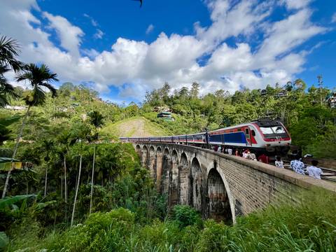       Passenger train crossing the iconic Nine Arches Bridge amid lush forest.
  