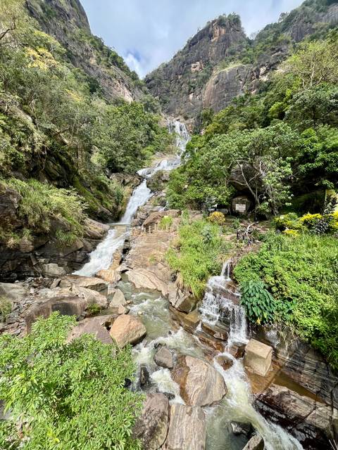       Multi-tiered hillside waterfall surrounded by dense greenery with visitors near the base.
  