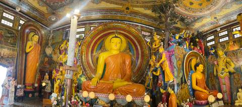       Vivid interior of a Buddhist temple dominated by a large seated Buddha and colourful murals.
  