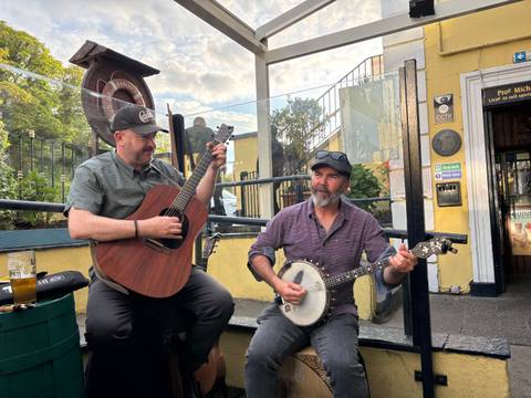       Two musicians playing guitar and banjo outside an Irish pub.
  