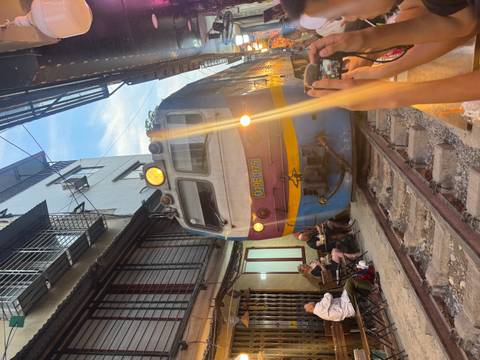       Close-up of locomotive squeezing past outdoor café tables as onlookers snap photos on Hanoi Train Street.
  
