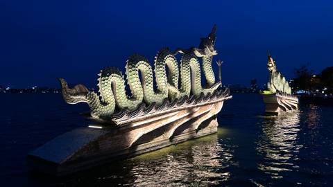       Illuminated dragon boat sculptures gleaming on calm water against a deep blue night sky.
  