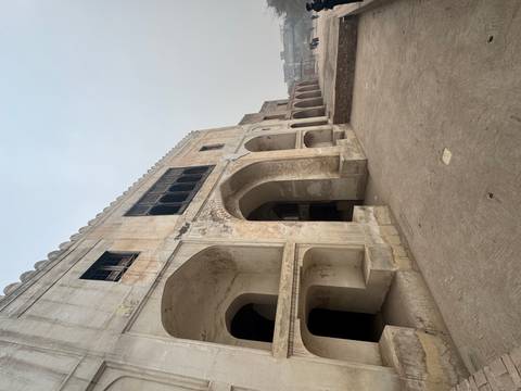       Weathered stone arches and corridors of an old Mughal-era fort on a hazy day.
  