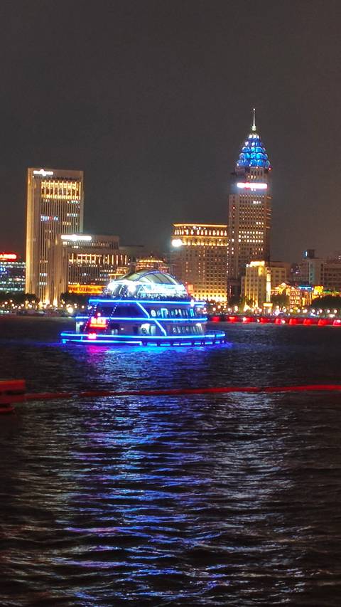      Neon-lit sightseeing boat gliding along a river against Shanghai’s illuminated skyline.
  