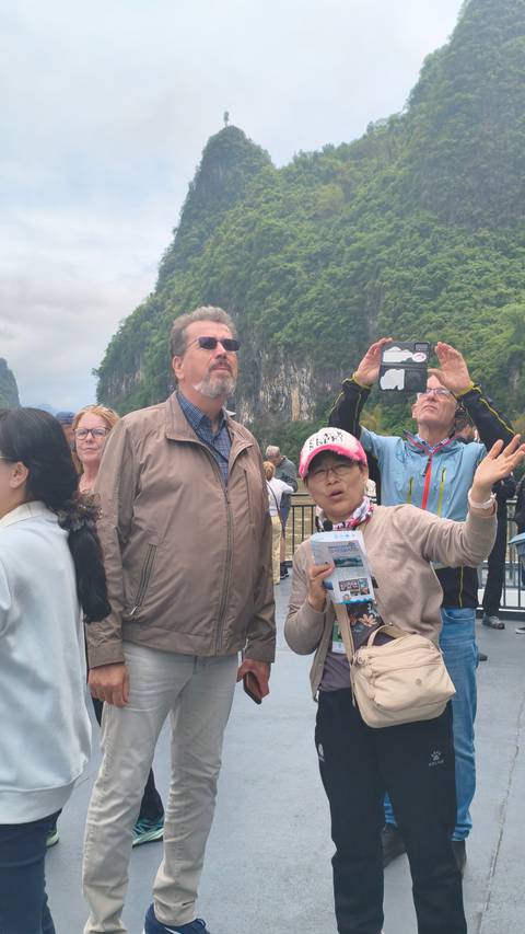       Tourists observe limestone cliffs along a river while guides explain the scenery.
  