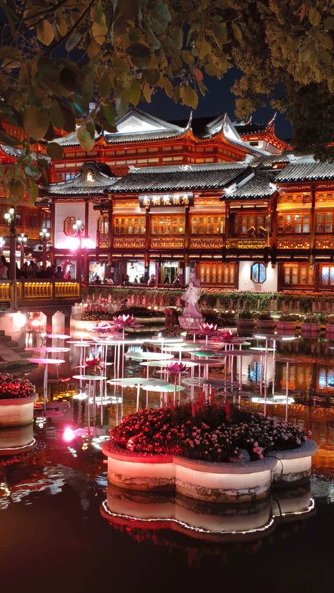       Lotus pond reflecting lantern lights in front of ornately lit pavilions at Yuyuan Garden.
  