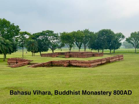       Low brick ruins of an ancient Buddhist monastery set in a broad green lawn.
  