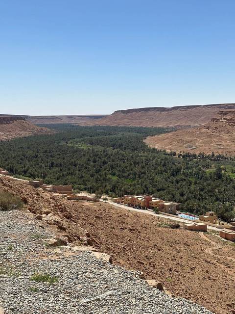       Expansive desert valley filled with a lush green palm oasis and scattered tan buildings between rocky hills.
  
