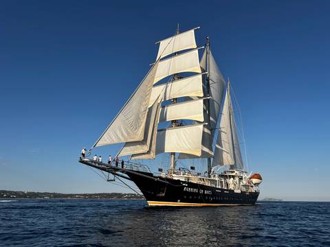       Close-up angle of tall ship with crew on bowsprit preparing sails
  