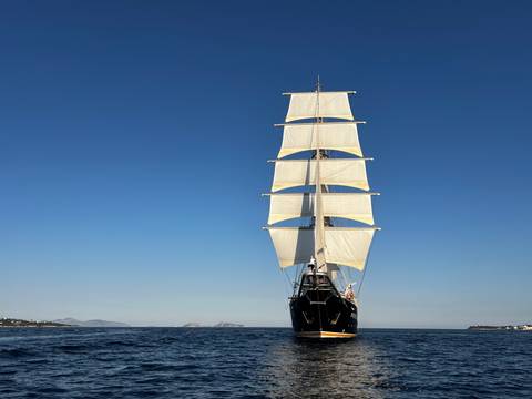       Front-on portrait of tall ship with full sails against a cloudless sky
  