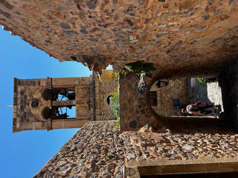       Stone bell tower overlooking a narrow arched passage in a historic Greek village
  