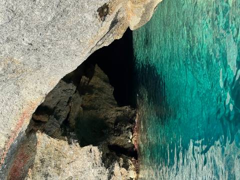       Turquoise water at the mouth of a rocky sea cave glinting in sunlight
  