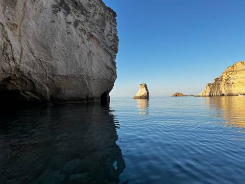       Serene coastal scene with towering rock cliffs and calm reflective water at golden hour
  