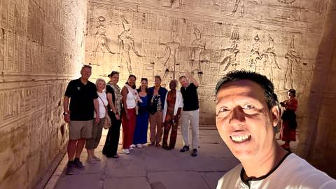      Small group stands inside an ornately carved ancient temple corridor illuminated by warm artificial light.
  