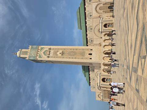       Imposing Hassan II Mosque minaret towers over a spacious marble plaza with scattered visitors.
  