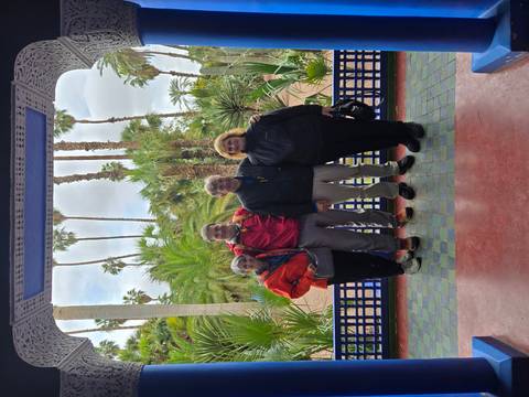       Four travellers stand in the lush Majorelle Garden framed by palm trees and colourful tiles.
  