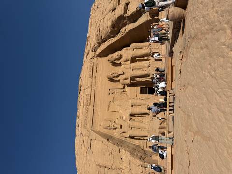       The colossal seated statues of Abu Simbel with many visitors exploring the forecourt under a deep blue sky.
  
