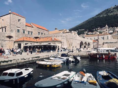       Dubrovnik’s old harbour with stone arches, moored boats and tourists strolling along the quay.
  