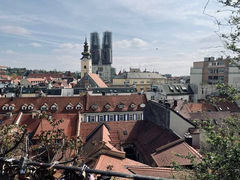       Rooftop view over Zagreb’s red-tiled houses toward the twin spires of the cathedral under renovation scaffolding.
  