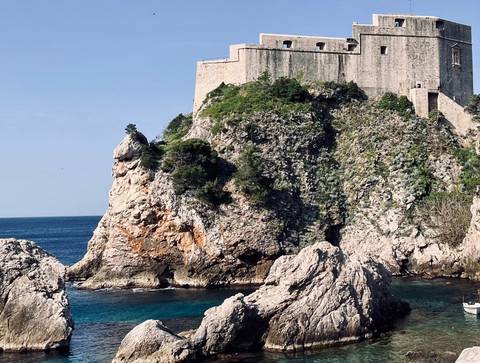       Stone fortification of Dubrovnik perched on a rugged cliff above the deep-blue Adriatic Sea.
  