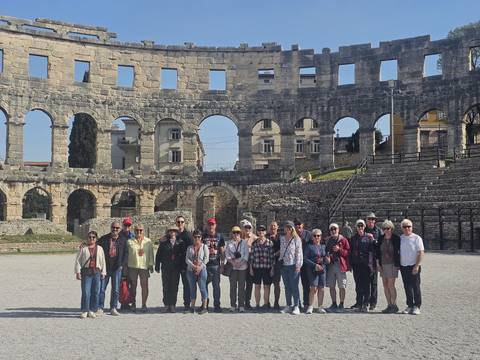      Large tour group posing inside the Roman amphitheatre surrounded by towering stone arches.
  