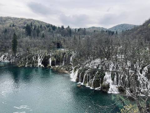       Series of cascading waterfalls tumble into a turquoise lake amid leafless forest at Plitvice.
  